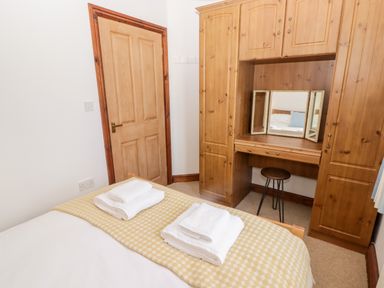A bedroom with a wooden wardrobe, dressing table with mirror, stool, bed with folded towels and a wooden door at Fountain Folly in Moylgrove near St Dogmaels