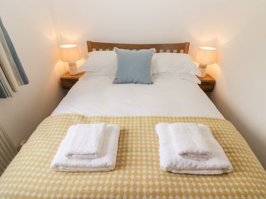 A bedroom with a double bed two bedside lamps and folded towels on a yellow patterned blanket at Fountain Folly in Moylgrove near St Dogmaels