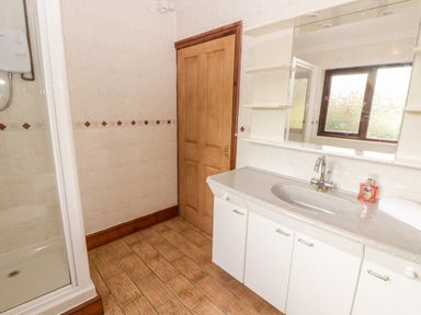 A bathroom with a shower cubicle a wooden door a large mirror a sink with a countertop and white cabinets Fountain Folly Moylgrove near St Dogmaels