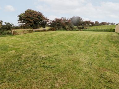 A grassy field with wooden fencing and trees at Fountain Folly in Moylgrove near St Dogmaels