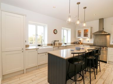 A kitchen with white cabinets a large island with three black stools and stainless steel appliances at Gorphwysfa in Llanddona near Beaumaris