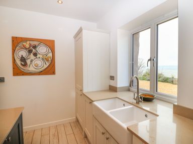 A kitchen with a double sink below a window and a painting on the wall at Gorphwysfa in Llanddona near Beaumaris