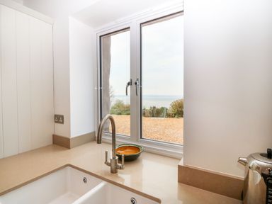 A kitchen sink with a faucet and a bowl on the counter near a window overlooking a gravel area and plants at Gorphwysfa in Llanddona near Beaumaris