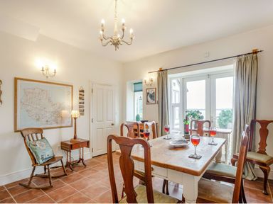 A dining room with wooden chairs and table with wine glasses a rocking chair and a map on the wall at Gorphwysfa in Llanddona near Beaumaris