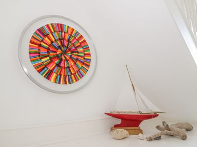 A room corner with a colorful circular artwork on the wall and a model sailboat on the floor surrounded by driftwood and coral at Gorphwysfa in Llanddona near Beaumaris