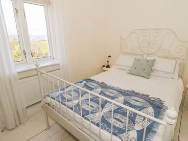 A bedroom with a white metal bed frame a blue patterned throw and window overlooking greenery at Gorphwysfa in Llanddona near Beaumaris