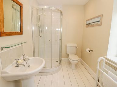 A bathroom with a corner shower, toilet, sink with mirror, and a towel rack at Gorphwysfa in Llanddona near Beaumaris