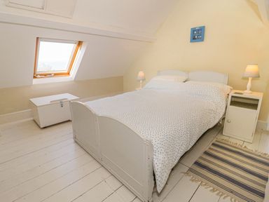 A bedroom with a white bed and bedside tables with lamps and a striped rug at Gorphwysfa in Llanddona near Beaumaris