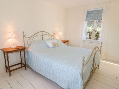 A bedroom with a metal bed frame two wooden bedside tables and a window with patterned blinds at Gorphwysfa in Llanddona near Beaumaris