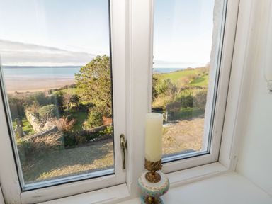 A window with a candle on the sill overlooking a garden and a beach at Gorphwysfa in Llanddona near Beaumaris
