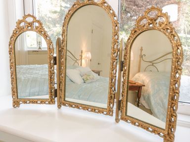 A three panel decorative mirror reflecting a bed with light blue bedding and a bedside table with a lamp at Gorphwysfa in Llanddona near Beaumaris