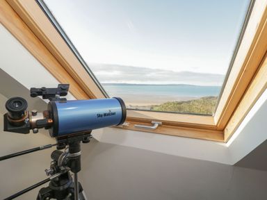 A telescope placed near a window with a view of the sea and coastline at Gorphwysfa in Llanddona near Beaumaris
