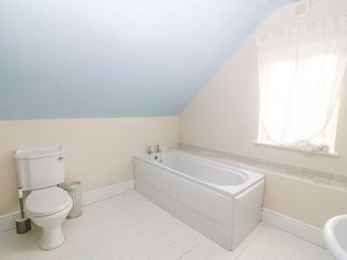A bathroom with a toilet and a bathtub under a sloped ceiling at Gorphwysfa in Llanddona near Beaumaris