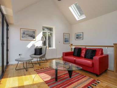 A living room with a red sofa black cushions a gray chair with a footrest and glass coffee table at Gorphwysfa in Llanddona near Beaumaris