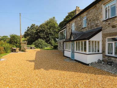 A stone house with a gravel driveway and an outdoor seating area surrounded by trees at Gorphwysfa in Llanddona near Beaumaris