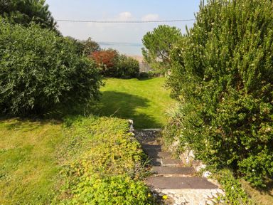A garden with stone steps leading down to a lawn surrounded by bushes and trees with a view of the sea at Gorphwysfa in Llanddona near Beaumaris