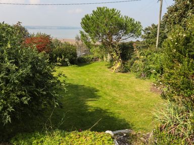 A garden with grass lawn trees and bushes overlooking a body of water at Gorphwysfa in Llanddona near Beaumaris
