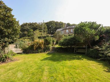A garden with a lawn a wooden bench a tree with a swing and a stone house in the background at Gorphwysfa in Llanddona near Beaumaris