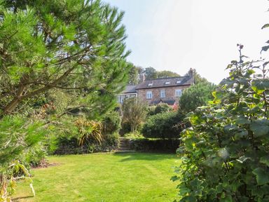 A garden with a lawn trees shrubs and a stone house in the background at Gorphwysfa in Llanddona near Beaumaris