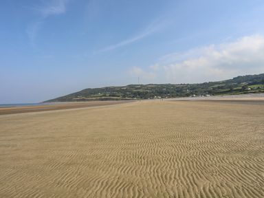 A wide sandy beach with ripple patterns and hills with houses in the background at Gorphwysfa in Llanddona near Beaumaris
