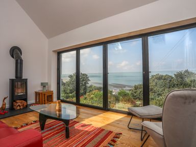 A living room with large windows overlooking a coastal view fireplace glass coffee table and red rug at Gorphwysfa in Llanddona near Beaumaris