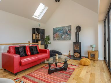 A living room with a red sofa black cushions a glass coffee table a fireplace and a skylight at Gorphwysfa in Llanddona near Beaumaris