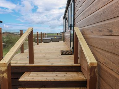 A wooden deck with glass railing and outdoor seating at Sandy Bay Retreat in Hasguard Cross near Broad Haven