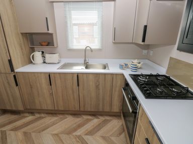 A kitchen with a sink toaster kettle gas stove oven wooden cabinets and a window at Sandy Bay Retreat in Hasguard Cross near Broad Haven