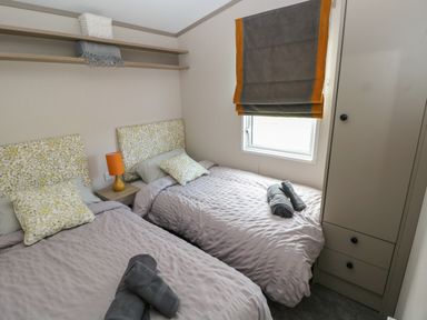 A bedroom with two single beds a bedside table with a lamp a window with a blind and a wardrobe at Sandy Bay Retreat in Hasguard Cross near Broad Haven