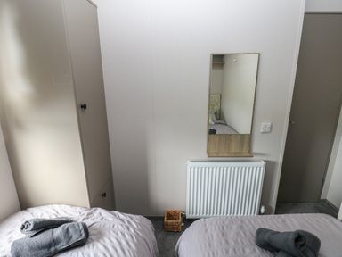 A bedroom with two single beds a wardrobe a wall mirror a radiator and folded towels at Sandy Bay Retreat in Hasguard Cross near Broad Haven
