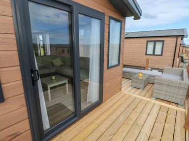 A wooden deck with wicker outdoor furniture and a sliding glass door to a room with a sofa and table at Sandy Bay Retreat Hasguard Cross near Broad Haven