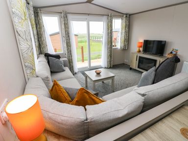 A living room with a corner sofa a small coffee table a TV on a cabinet and windows with curtains at Sandy Bay Retreat in Hasguard Cross near Broad Haven