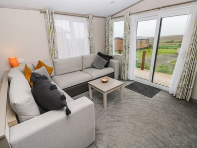 A living room with a sectional sofa and pillows next to sliding glass doors at Sandy Bay Retreat in Hasguard Cross near Broad Haven