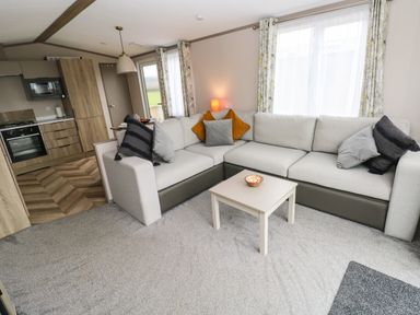 A living room with a corner sofa and coffee table next to a kitchen area at Sandy Bay Retreat in Hasguard Cross near Broad Haven