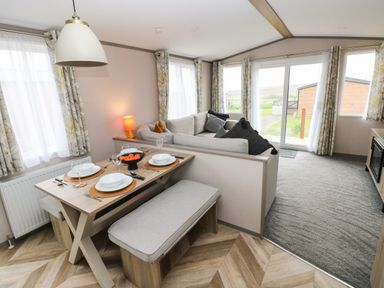 A dining area with a table set for four and a living room with a sectional sofa and sliding glass doors at Sandy Bay Retreat in Hasguard Cross near Broad Haven