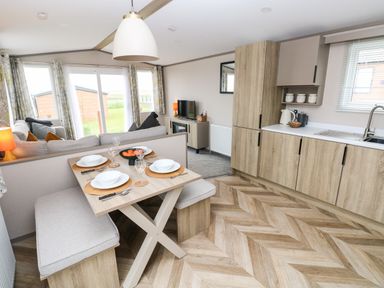 A kitchen and dining area with a table set for four and a living room with a sofa and television at Sandy Bay Retreat in Hasguard Cross near Broad Haven