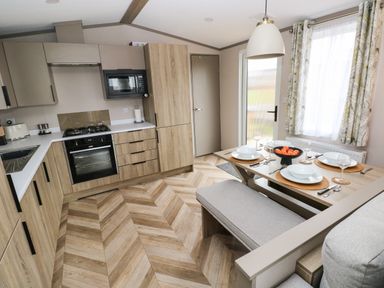 A kitchen and dining area with wooden cabinets wooden floor a dining table set with plates bowls cutlery and glasses at Sandy Bay Retreat in Hasguard Cross near Broad Haven