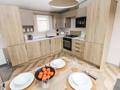 A kitchen with wooden cabinets and a dining table set with white plates and glasses at Sandy Bay Retreat in Hasguard Cross near Broad Haven