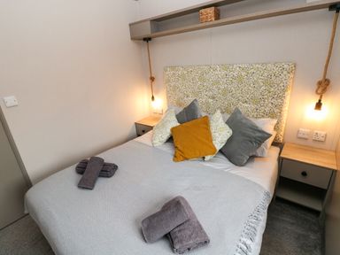 A bedroom with a bed with patterned headboard and pillows beside two bedside tables with hanging lights at Sandy Bay Retreat in Hasguard Cross near Broad Haven
