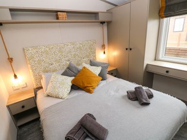 A bedroom with a double bed pillows and towels bedside tables lamps a window and a wardrobe at Sandy Bay Retreat in Hasguard Cross near Broad Haven