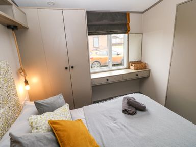 A bedroom with a bed and pillows a window with a curtain a wardrobe and a desk with drawers Sandy Bay Retreat Hasguard Cross near Broad Haven