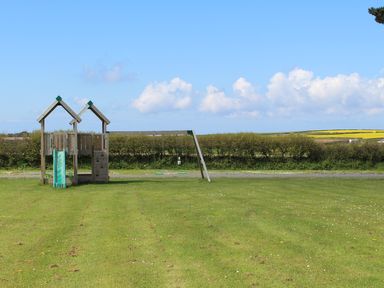 A playground with swings and a slide on a grassy field with hedges and farmland in the background at Sandy Bay Retreat in Hasguard Cross near Broad Haven