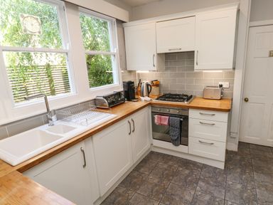 A kitchen with white cabinets wooden countertops a gas stove an oven a stainless steel sink and large windows at 8 Rosewall Cottages in St Ives