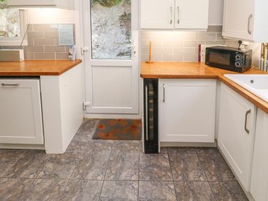 A kitchen with white cabinets wooden countertops a microwave a sink a door and a floor mat at 8 Rosewall Cottages in St Ives