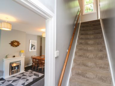 A stairway with carpet and wooden handrail next to a dining room with wooden table chairs and fireplace at 8 Rosewall Cottages in St Ives