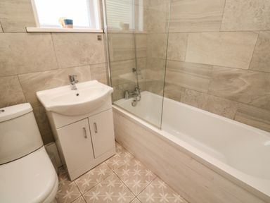A bathroom with a toilet sink vanity unit and bathtub with glass shower screen at 8 Rosewall Cottages in St Ives