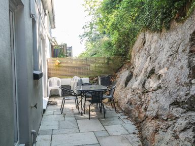 A small outdoor patio with a table and chairs next to a rock wall at 8 Rosewall Cottages in St Ives