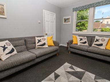 A living room with two gray sofas with decorative pillows a geometric patterned rug and a window at 8 Rosewall Cottages in St Ives