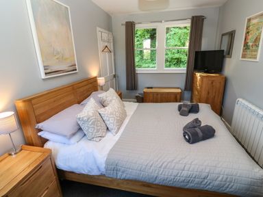 A bedroom with a wooden bed with pillows and towels near a window and wooden furniture at 8 Rosewall Cottages in St Ives