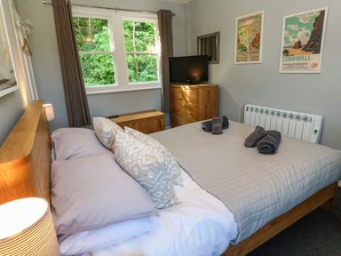 A bedroom with a bed with pillows and folded towels next to a window and a wooden dresser with a television at 8 Rosewall Cottages in St Ives
